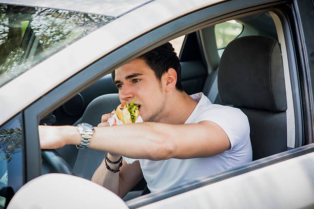 istock Young man driving his car while eating food 478860940