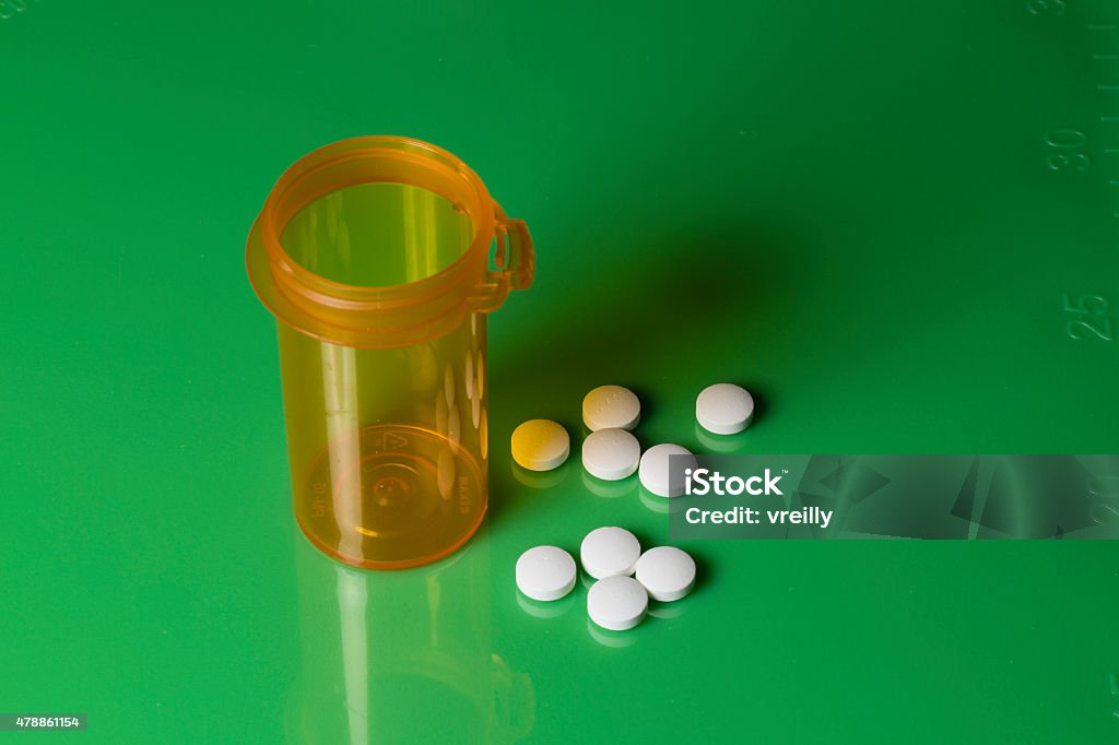 Pill Bottle and Pills on a Green Scaled Slab A pill bottle and white tablets scattered on a green board with an inches scale along the side 2015 Stock Photo