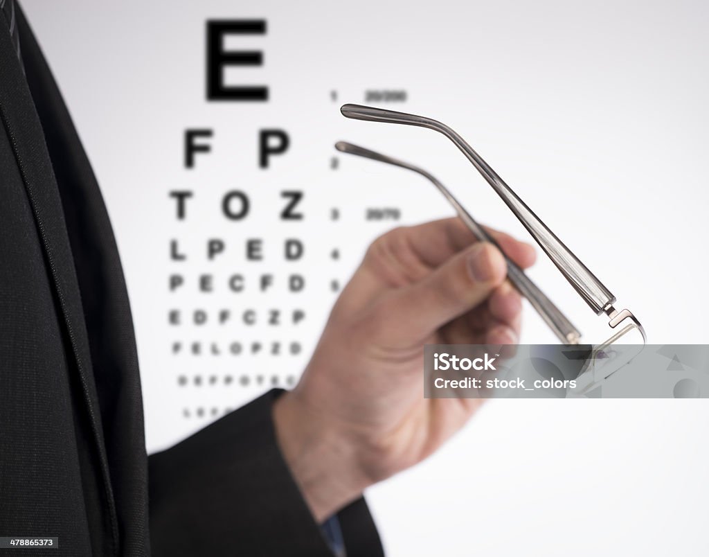 oftalmology side view of man holding eyeglasses, eyechart in background. Lens - Eye Stock Photo