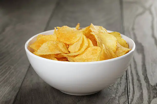 organic potato chips in white bowl on wood table, close up