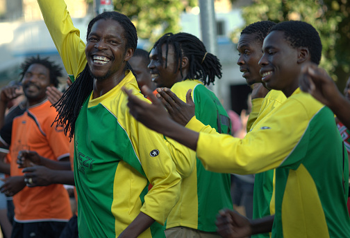 Edinburgh, Scotland, UK - August 10, 2012: African/Zambezi street dance/music group at the Edinburgh festival. Central figure in green and yellow dancing and smiling at the camera, others with hands raised and clapping, background figures in same top, others on the left in orange