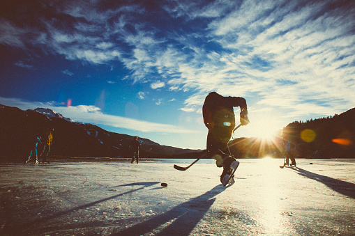 Playing ice hockey on frozen lake in sunset.