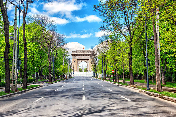 Arch of Triumph, Bucharest, Romania Arch of Triumph, Bucharest, Romania. Initially built of wood in 1922 to honor the bravery of Romanian soldiers who fought in World War I, Bucharest's Arc de Triomphe was finished in Deva granite in 1936. Designed by the architect, Petre Antonescu. Empty street in the morning with many trees in the park, leading to the Triumph Arch - landmark in Bucharest, romanian capital bucharest photos stock pictures, royalty-free photos & images