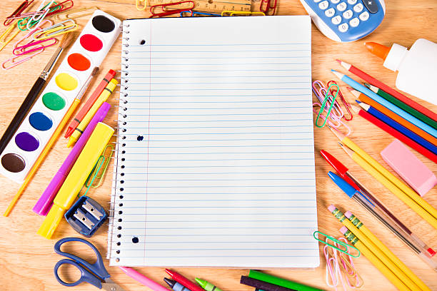 Back to school. Pile of school supplies with open notebook. It's back to school time!  A large pile of elementary school supplies with a white, blank open notebook for copyspace. Supplies include: calculator, paints, pencils, markers, pens, erasers, crayons and more.  The supplies are laying on a school desktop.  Education themes.  Directly above view. classroom empty education desk stock pictures, royalty-free photos & images