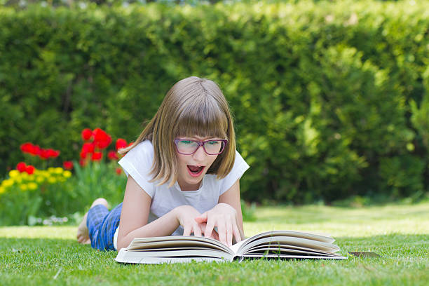 Thoughtful Teenage Girl With Book Sitting On Grass Against Sky