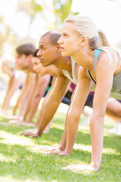 Woman With Friends Doing Push-Ups In Park Side view of young woman with friends doing push-ups in park. Vertical shot. military camp stock pictures, royalty-free photos & images
