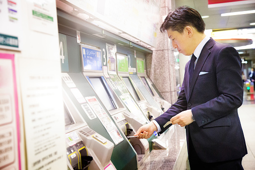 Japanese businessman buying a Tokyo subway ticket / recharging his IC card at automatic teller. He is well dressed in a suit.