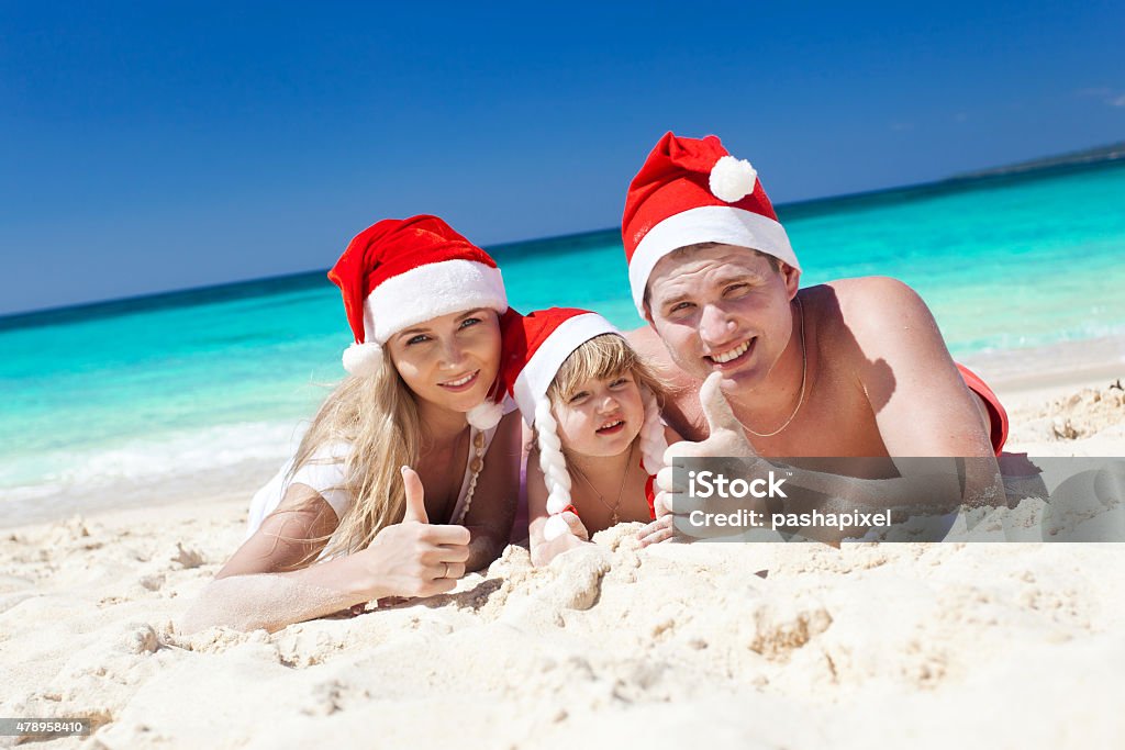 Happy family on beach in Santa hats, celebration christmas Happy family on beach in Santa hats, mother, father and little daughter. 2015 Stock Photo