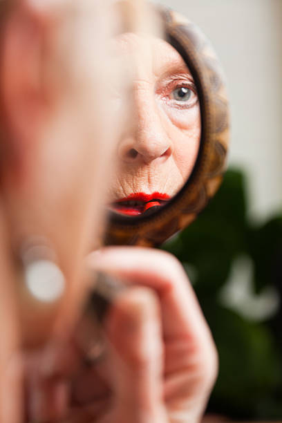 istock Good looking senior woman doing lipstick in front of mirror. 478967711