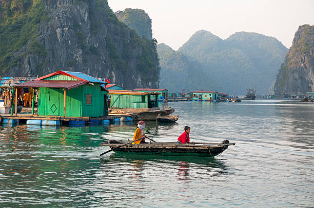 Cat Ba Island, Halong Bay, Vietnam - December 21, 2006: A woman and child rowing a small boat near the floating homes around Cat Ba Island in Halong Bay, Vietnam. There is a large community of people living in floating house boats around Cat Ba Island.