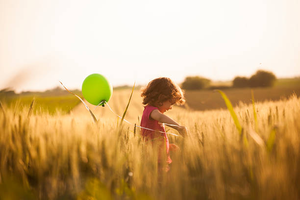 Cute little girl with balloons at field Cute little girl holding balloons and running through field charming photos stock pictures, royalty-free photos & images