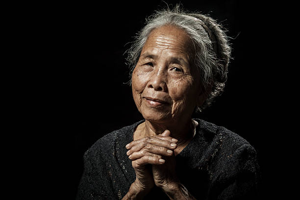 vecchia donna pregare su sfondo nero - povertà asia foto e immagini stock