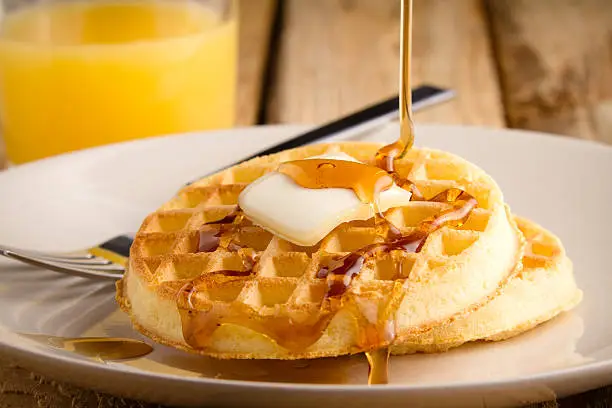 This s a photo of a couple waffles being soaked in syrup. Shot on a wooden table with a shallow depth of field.