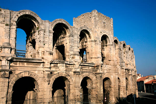 Roman amphitheater / Arena of Arles, Bouche-du-Rhône Dpt, France. Rivaled only by the Roman amphitheater in Nîmes, the Arena (Amphitheater) dominates old Arles. It seats over 21,000 spectators and still hosts bullfights in summer. Dating probably from early in the A.D. first century. The amphitheater's four medieval towers are testimony to its transformation from classical sports arena to feudal fortification in the Middle Ages.  With a length of 136 m and a width of 107 m the arena was one of the largest in Gaul. The facade has a double row of arcades with 60 archways each 3.38 m wide; the four arches used as main entrances are 4.80 m wide. beziers stock pictures, royalty-free photos & images