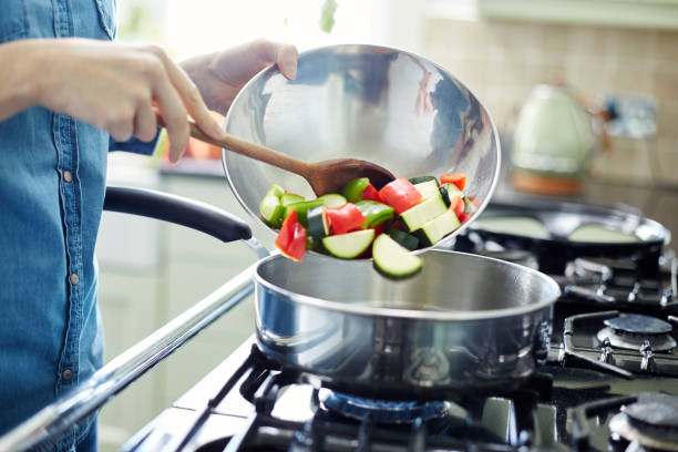 Woman adding chopped vegetables into saucepan Midsection of woman adding fresh chopped vegetables in saucepan. Utensil is placed on gas stove. Close-up of female holding container and wooden spoon. She is preparing food in domestic kitchen. gas stove burner photos stock pictures, royalty-free photos & images