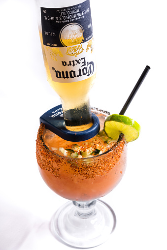 Los Angeles, Сalifornia, USA - October 20, 2014: Michelada cocktail with Corona Beer on white background. Michelada is a Mexican cerveza preparada made with beer, lime juice, and assorted sauces, spices, and peppers. It is served in a chilled, salt-rimmed glass. There are numerous variations of this beverage throughout Mexico and Latin America.  Corona Beer is made by Cervecerias Modelo in Mexico.
