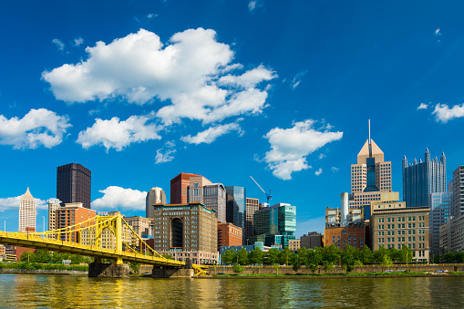 Pittsburgh downtown skyline with Allegheny River and the Roberto Clemente Bridge / Sixth Street Bridge in the foreground and puffy cumulus clouds in the background.