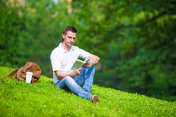 istock Young man relaxing with coffee in park reading a book 479061084