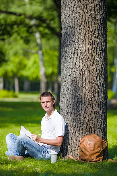 istock Young man relaxing near tree with coffee reading a book 479070134