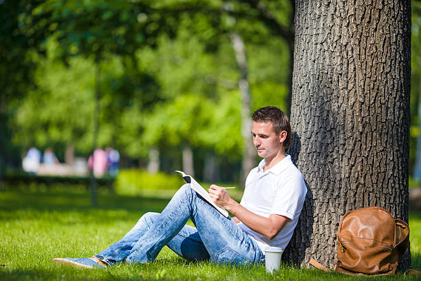istock Young man relaxing near tree with coffee reading a book 479070136