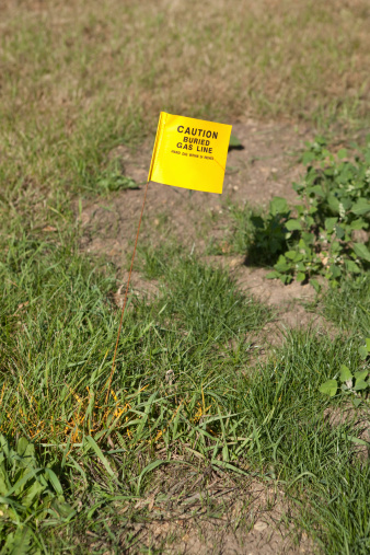A Caution Buried Gas Line flag and yellow spray painted stripe on grass at a construction site.