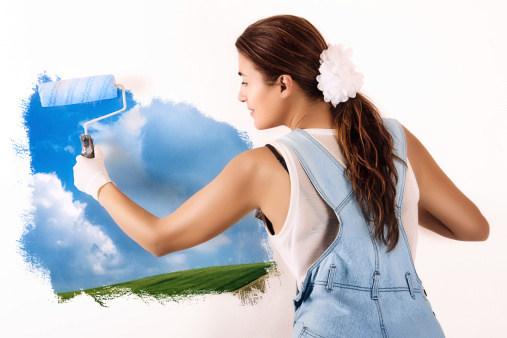 Young woman painting a nature landscape on wall with roller. Mural painting on wall. Ecologist