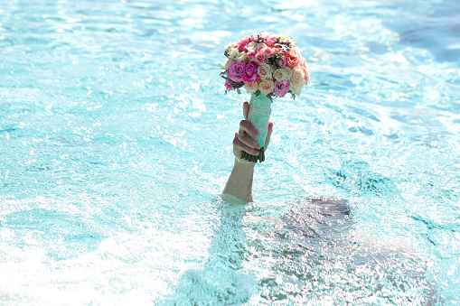 Male in swimming pool with blue water holding beautiful fresh wedding bunch of pink lilac purple white and violet chrysanthemum rose and peony flowers in hand copyspace, horizontal picture
