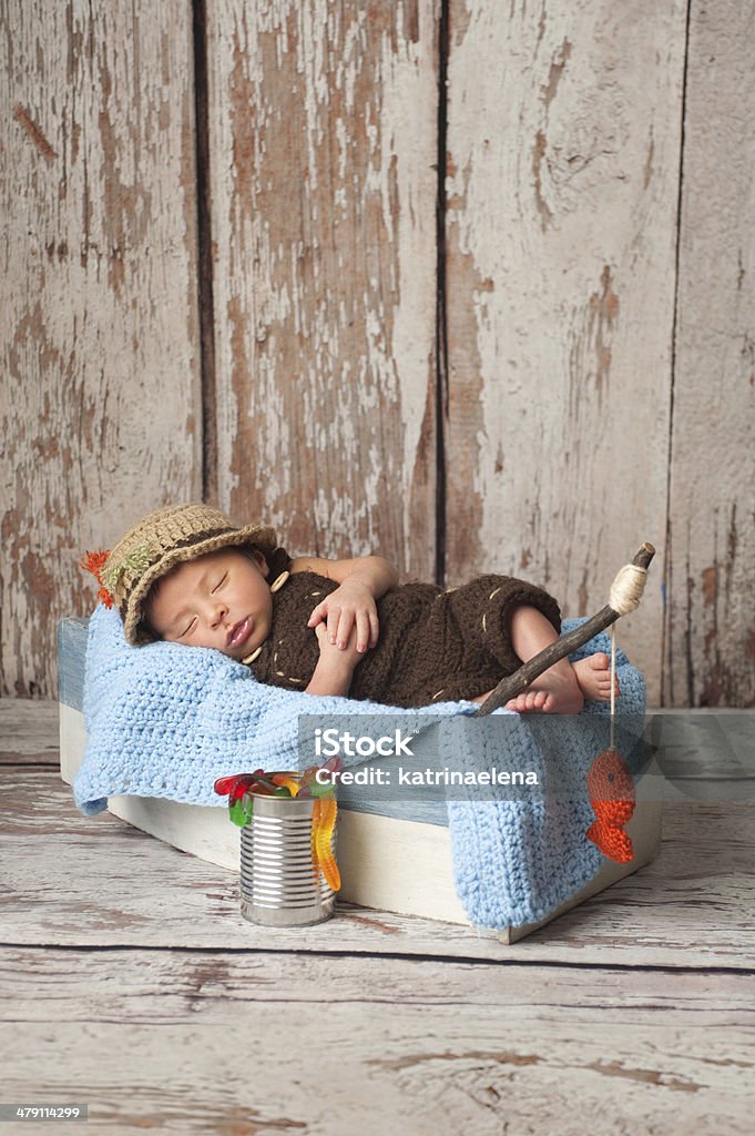Newborn Baby Boy in Fisherman Outfit Portrait of a nine day old newborn baby boy. He is sleeping in a miniature boat and wearing crocheted overalls and a fisherman's hat. Shot in the studio on a rustic wood background. 0-11 Months Stock Photo