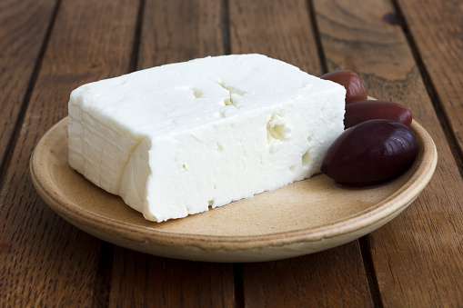 Greek feta cheese with kalamata olives on rustic plate and table.