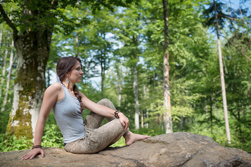 Young woman with long brown hair relax on a rock in a forest in europe
