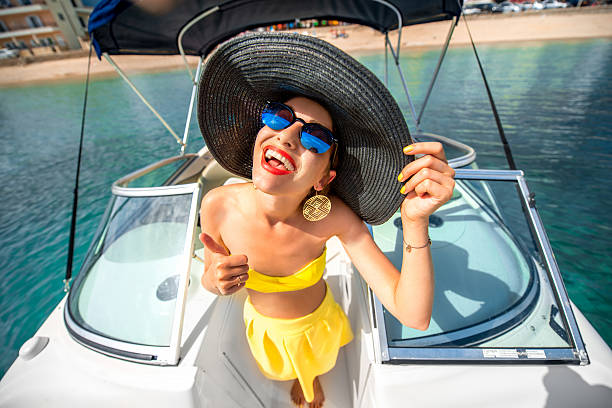 Young playful woman with big hat and sunglasses having fun on the yacht. Happy summer vacation. Top view with wide angle 