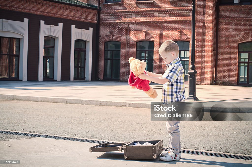kid is opening the suitcase and taking teddy bear toy little kid is opening the suitcase on the sunny street in the morning, holding teddy bear 2015 Stock Photo