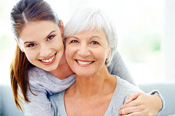 An attractive young woman smiling alongside her senior mother