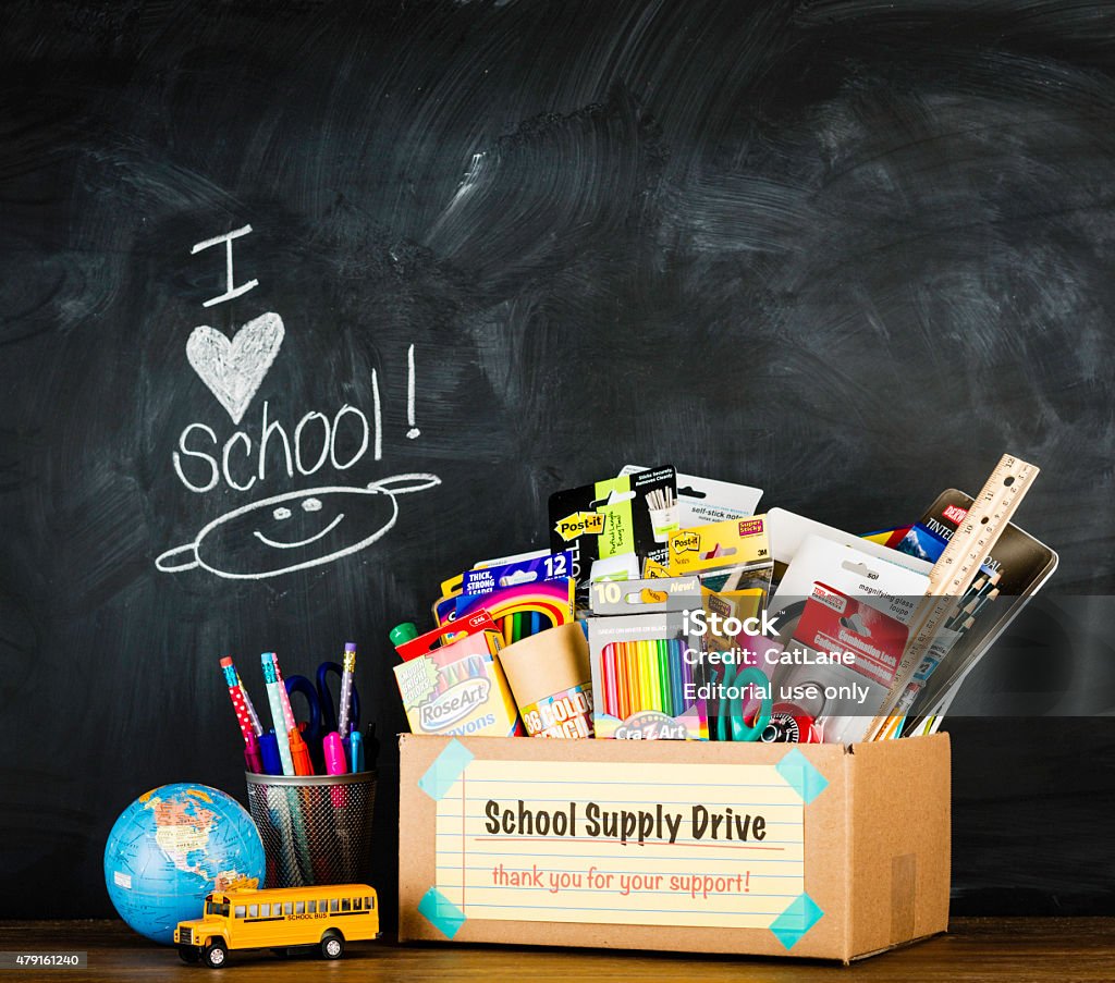 Donation Box for School Supplies Suffolk, Virginia, USA - August 22, 2013: A horizontal studio shot of a a donation box for school supplies shot against an authentic school chalkboard. The box is filled with assorted school supplies and essentials. Next to the box is a miniature school bus, world globe and a collection of new pens and pencils. Equipment Stock Photo