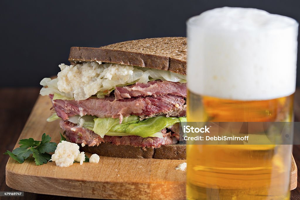 Beer And A Corned Beef Sandwich A close up shot of a glass of beer and an oversized corned beef sandwich on dark rye in the background. St. Patrick's Day Stock Photo