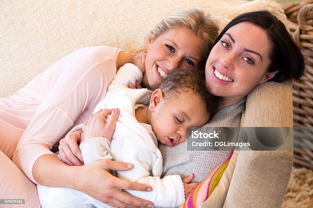 Female couple cuddling with their baby son Same sex female couple lying down with their baby son Lesbian Stock Photo