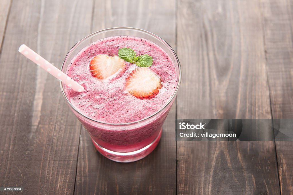 Strawberry fruit smoothies with straw on wooden background. Strawberry smoothie and fresh strawberries in glass on wooden background 2015 Stock Photo