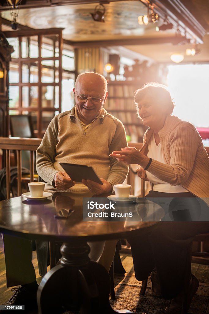 Smiling seniors using digital tablet in a cafe. Happy senior couple sitting in a cafe and using touchpad together. 2015 Stock Photo