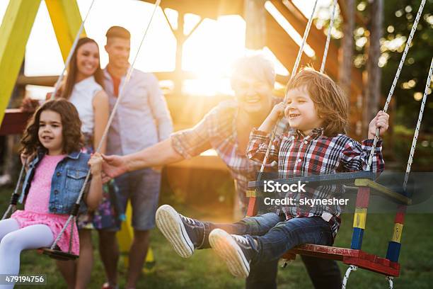 Grandmother Swinging Her Grandchildren At Sunset Stock Photo - Download Image Now - Playground, Child, Grandparent