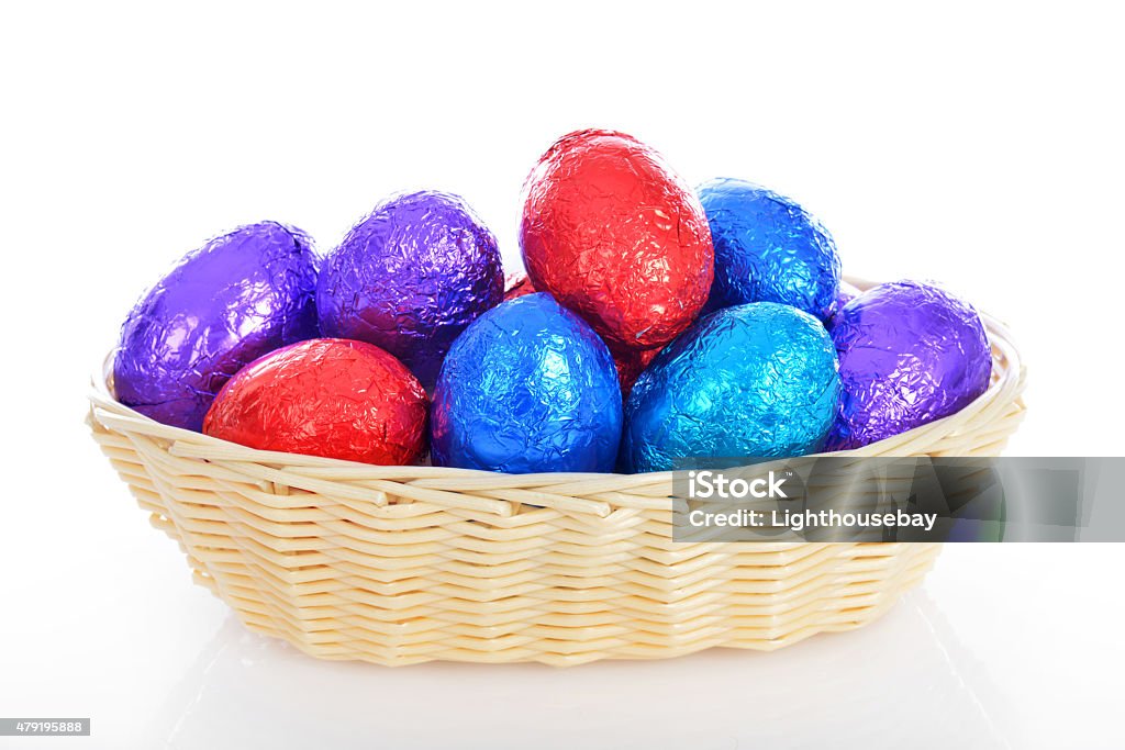 Wicker basket of multi coloured chocolate easter eggs white background A wicker basket of multi coloured chocolate easter eggs white background 2015 Stock Photo