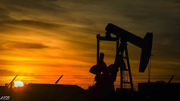 The silhouette of a pump jack looms over a rising sun.