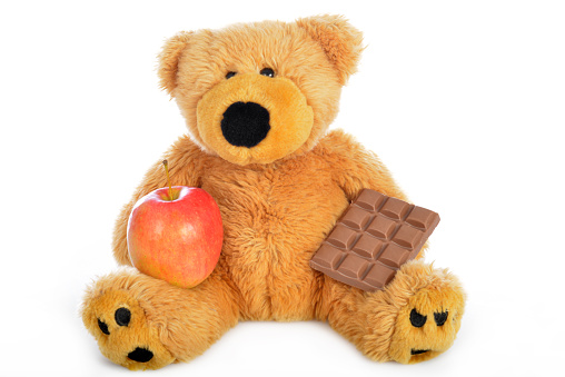 Teddy bear sitting and holding chocolate and an apple on white background, Horizontal image.