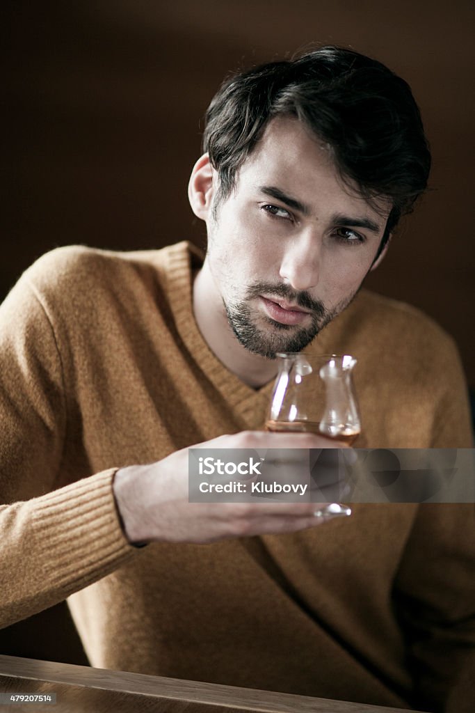 Young man with a glass of brandy Young handsome man sitting with a glass of brandy in his hand. He is wearing a yellow sweater. 20-29 Years Stock Photo