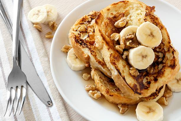 French toast with bananas, walnuts and maple syrup Plate of delicious French toast with bananas, walnuts and dripping maple syrup, overhead view french toast stock pictures, royalty-free photos & images