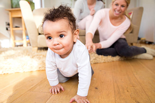 Baby boy crawling at home Female couple watch proudly as their baby son crawls along the floor crawling photos stock pictures, royalty-free photos & images