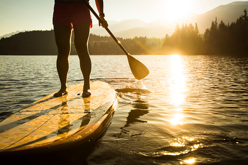 Silhouette of young Asian female paddle boarding in calm waters. Horizontal photograph with lens flare.