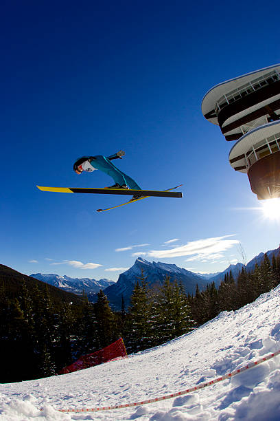 CLOSE UP: Stunning view of freestyle skier doing grab trick while jumping kicker. Young extreme athlete flying high above snow park and ski area. Adrenaline activity on sunny winter day in ski area.