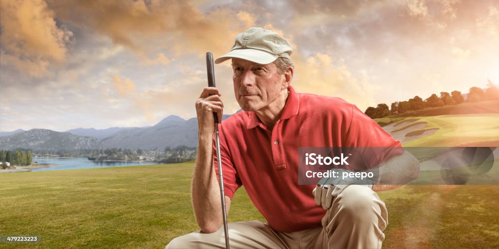 Golfer Weighing Up a Shot Close up portrait image of mature male golfer wearing polo shirt and cap, squatting down holding club contemplating next shot on golf course at sunset Golf Stock Photo