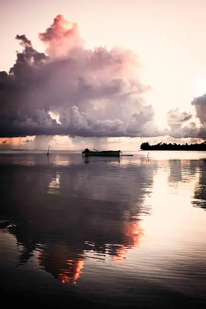 An outrigger canoe is silhouetted in a pink sunset on Maupiti, French Polynesia