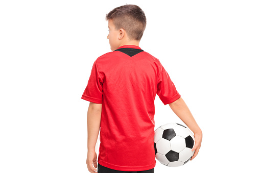 Junior soccer player holding a ball isolated on white background, rear view